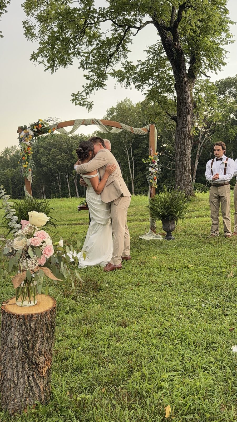 Bride and groom embracing under a floral arch at an outdoor ceremony